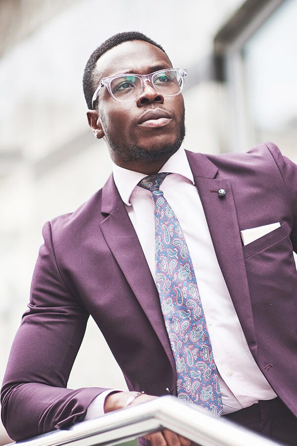 A man in purple suit and glasses standing outside.