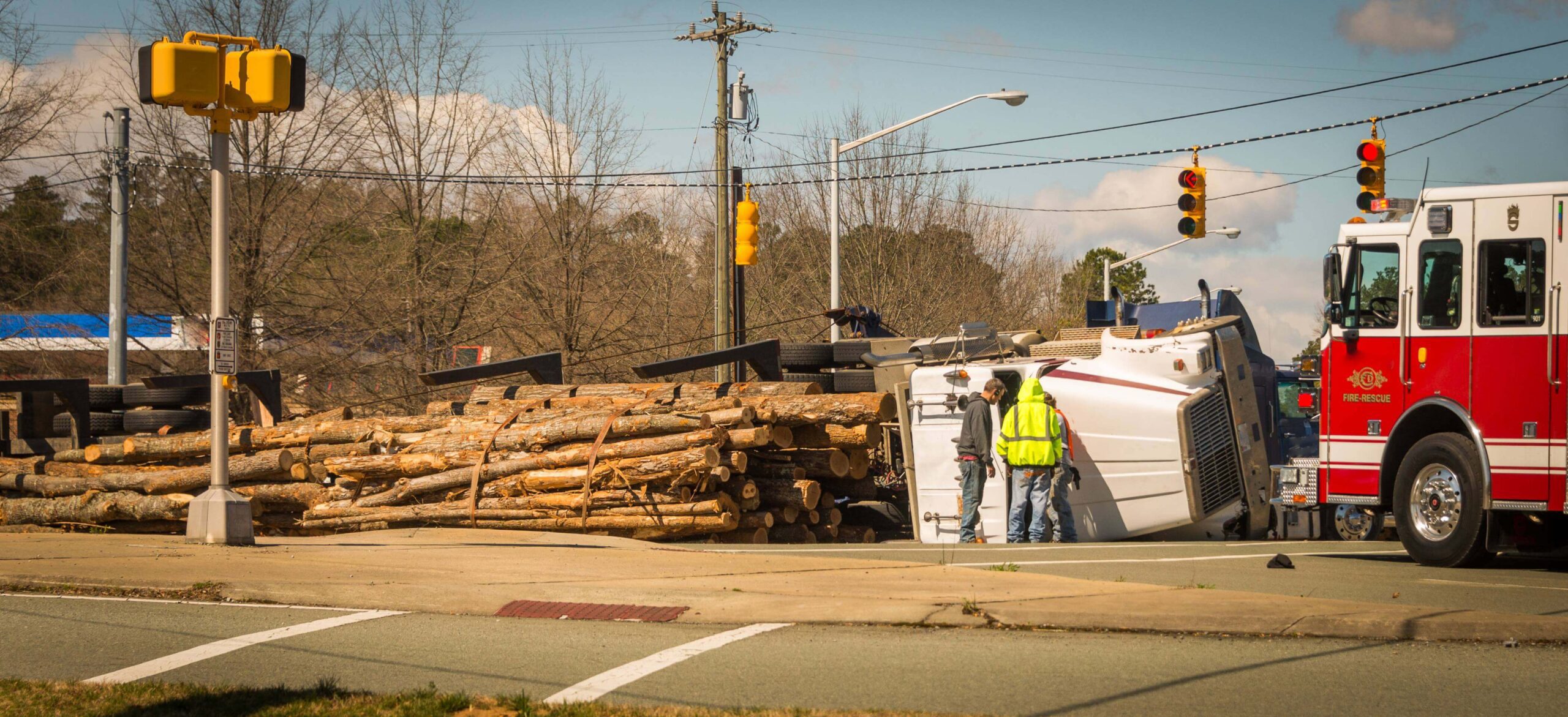 A man in yellow vest standing next to a pile of wood.